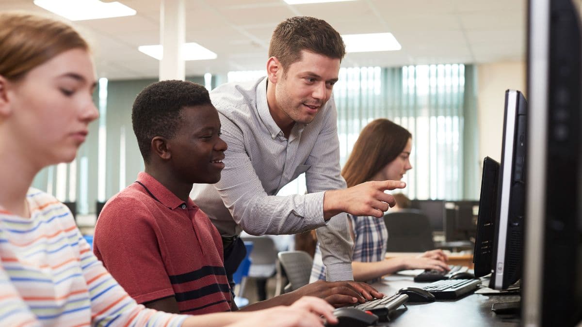 Instructor helping students at computers in a classroom lab.