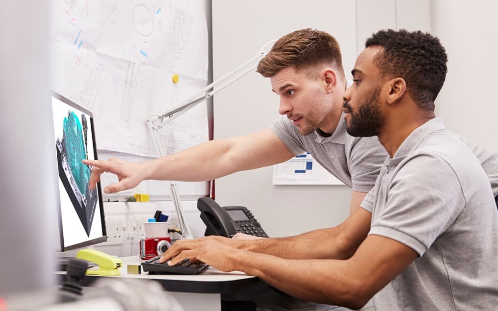 Two engineers collaborating on a CAD model at a monitor.